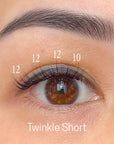 Close-up of an eye with short press on eyelashes labeled 'Twinkle Short' on a beige background